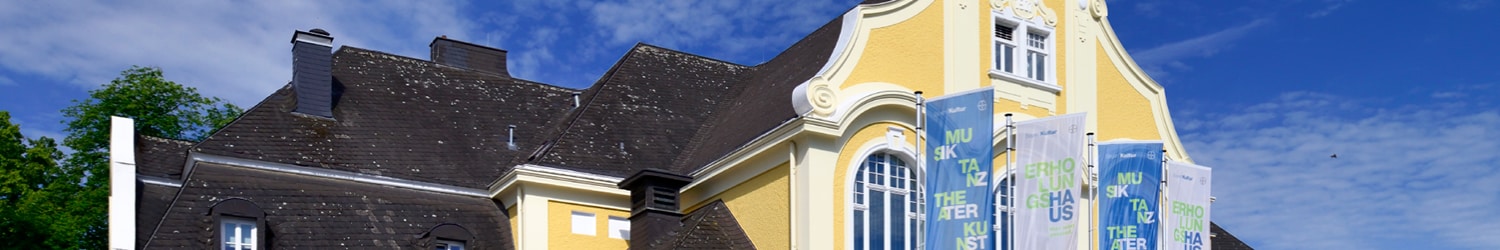 A large yellow building with dark roofs and several colorful vertical banners on the facade against the backdrop of a blue sky.