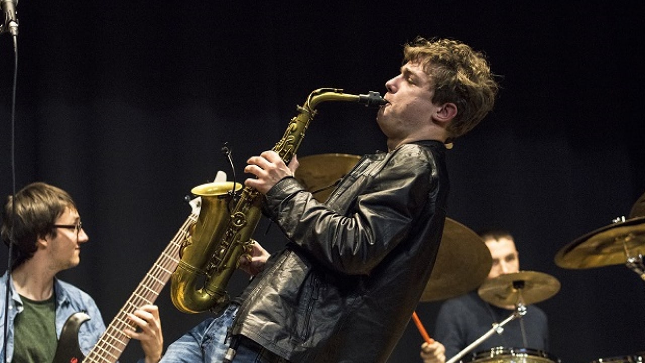 Auf der Bühne spielt ein Mann energisch Saxophon, begleitet von einem Bassisten und einem Schlagzeuger.