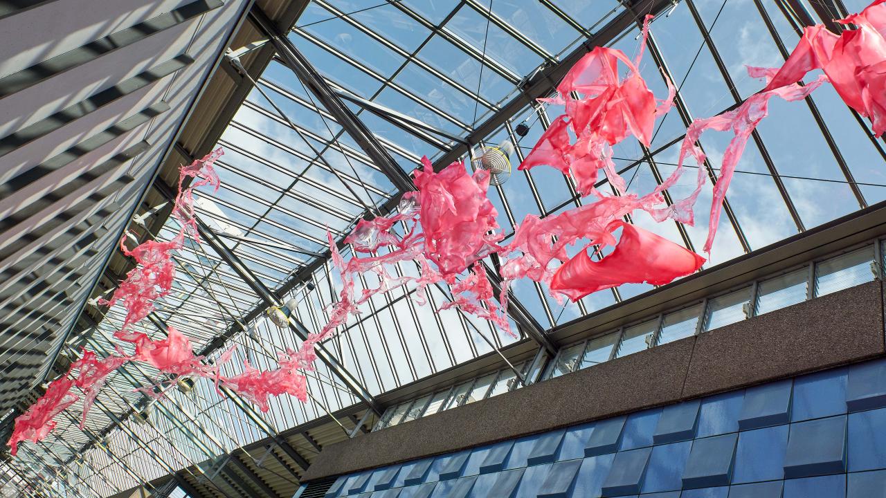Rote abstrakte Skulptur, die von der modernen Glasdecke eines Gebäudes mit geometrischer Architektur hängt.
