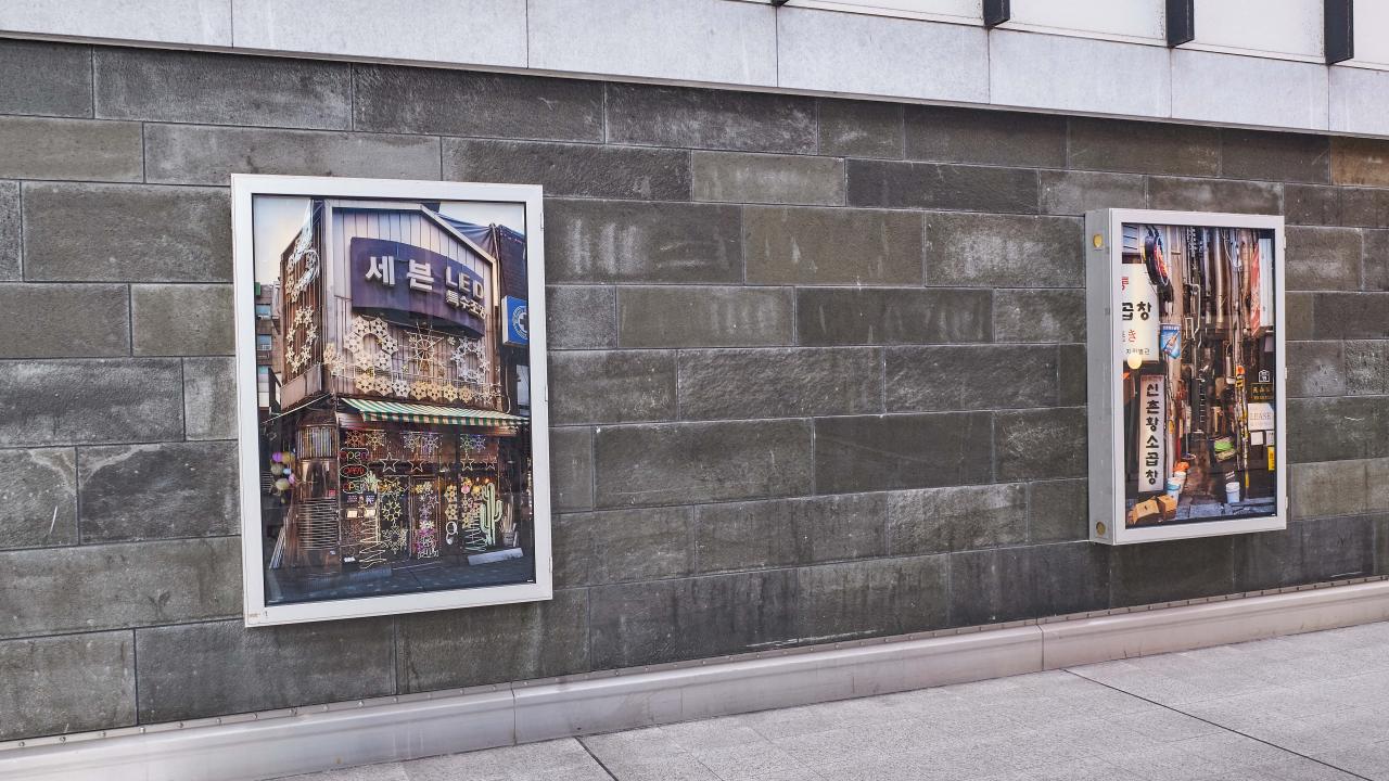 Auf einer grauen Steinwand hängen zwei gerahmte Fotografien belebter Stadtstraßen.